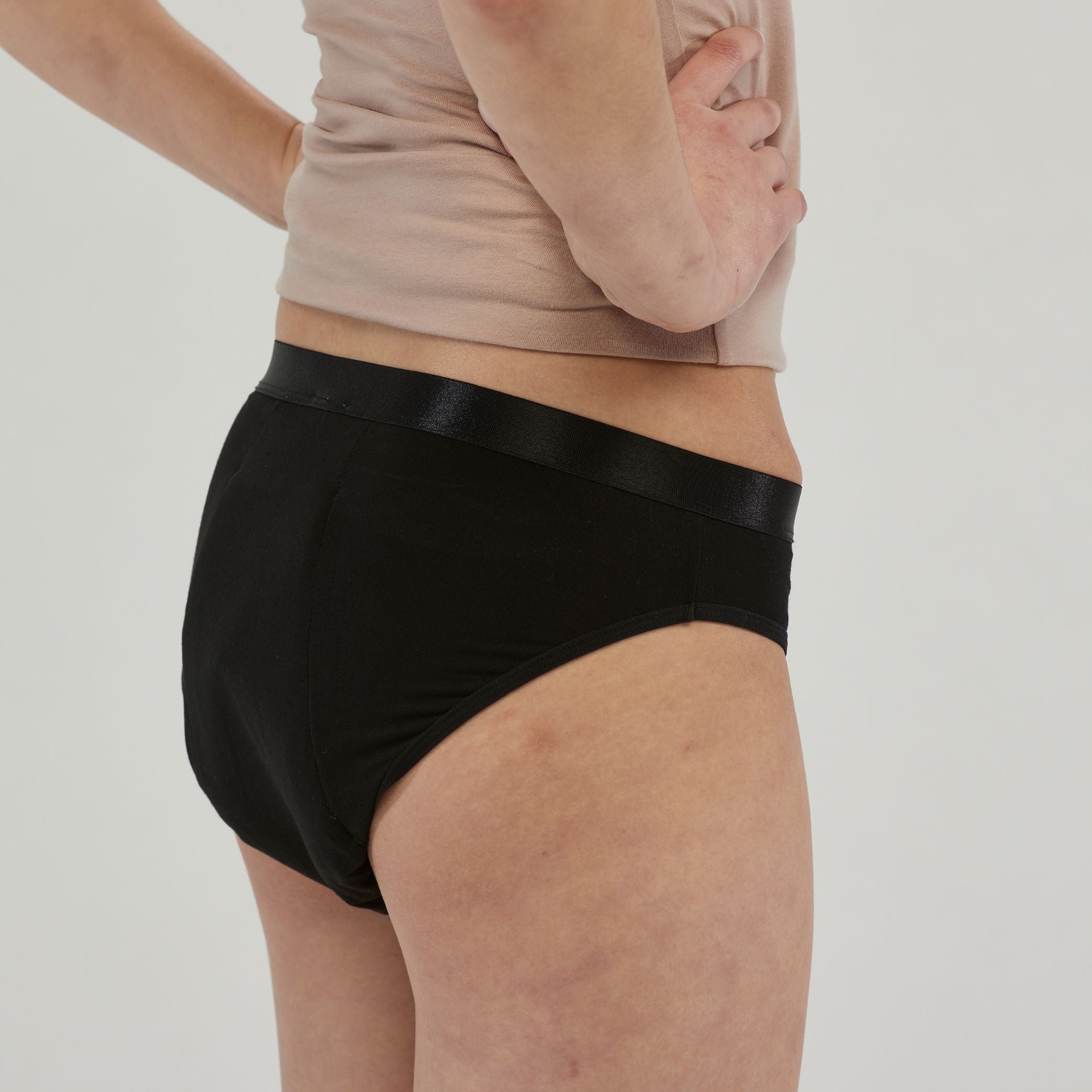 Side view of a woman wearing black waterproof incontinence hipster underwear, offering leak-proof protection with a sleek, comfortable fit. Designed for discreet wear and everyday confidence.