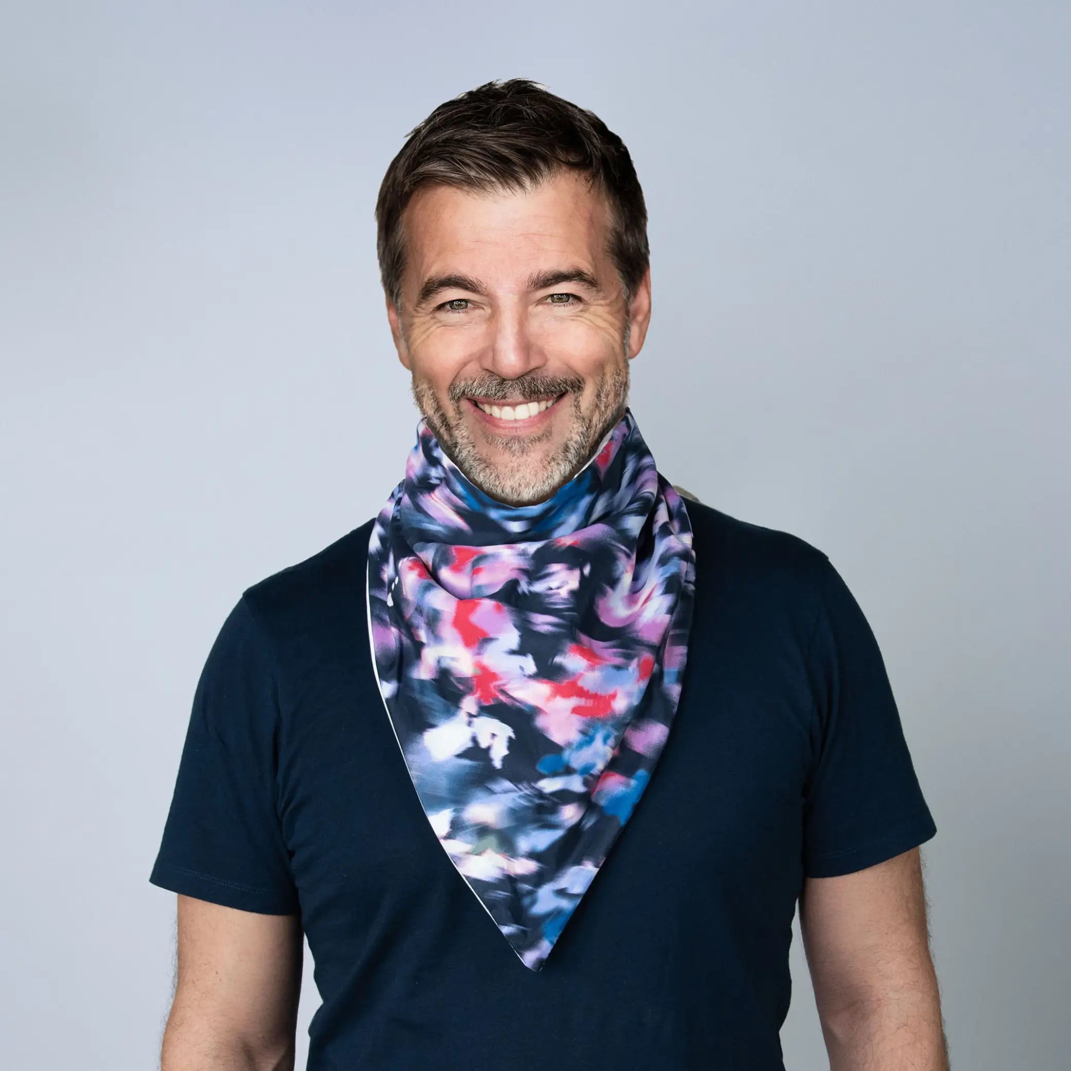 Smiling man wearing a stylish StayDry absorbent and waterproof bandana bib with a vibrant abstract pattern