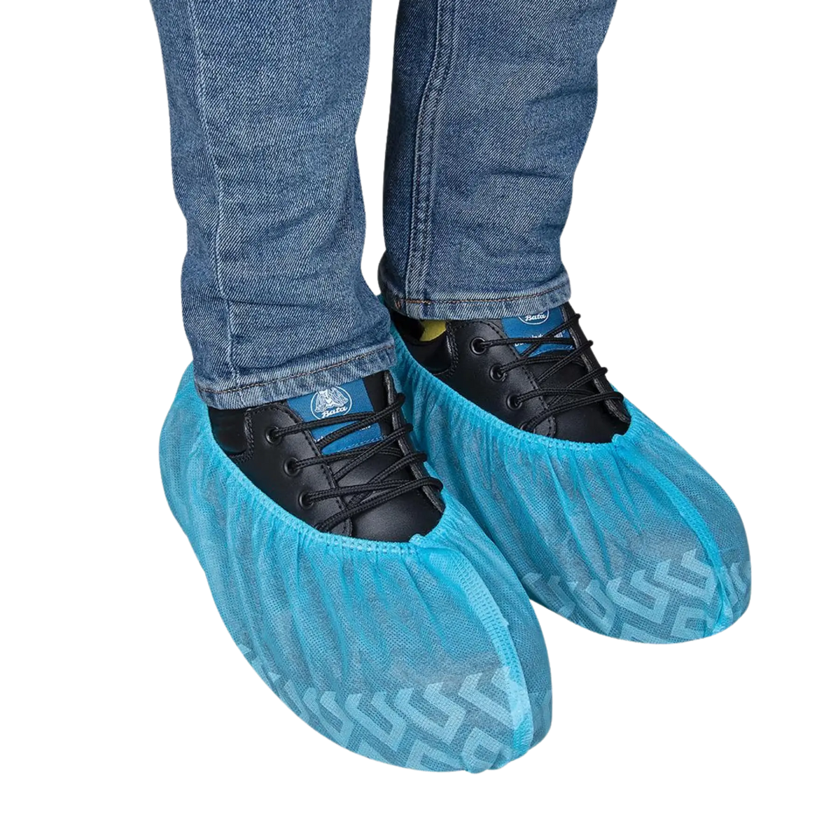 Pair of light blue disposable non-skid SPP shoe covers with printed tread patterns, fitted over black safety work shoes and blue jeans, on a transparent background.