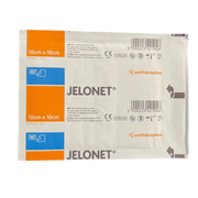 Close-up of two sterile, individually wrapped sachets of Smith & Nephew Jelonet Paraffin Gauze Dressing, size $10 \text{ cm} \times 10 \text{ cm}$.